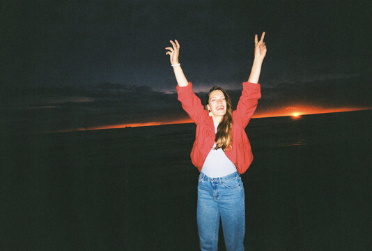 Woman Stands at the Beach With Arms Raised During Sunset