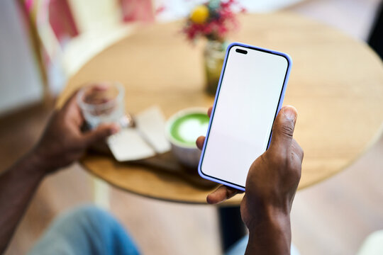 Hands holding smartphone with blank screen in cafe