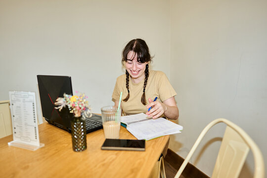Person laughing studying with laptop and notebook in cafe