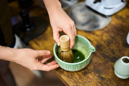 Hands whisking matcha tea in traditional ceremony bowl
