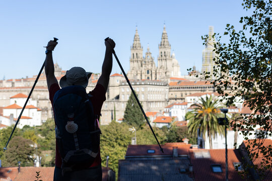 silhouette of pilgrim on camino de santiago raising hiking poles looking at cathedral of santiago celebrating arrival