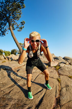 Man adjusts sunglasses while posing on rocky terrain