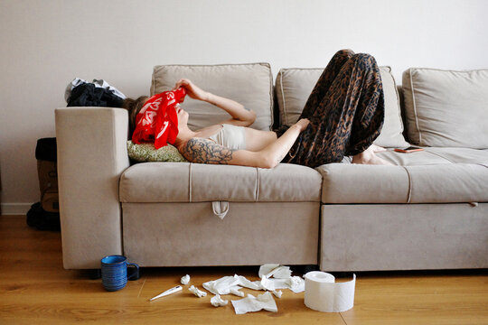 Person lying ill on couch with tissues scattered on floor