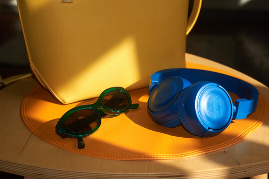 Sunglasses, blue headphones and yellow bag on orange placemat