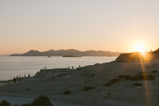 Sun sets over silhouetted coastline, Milos