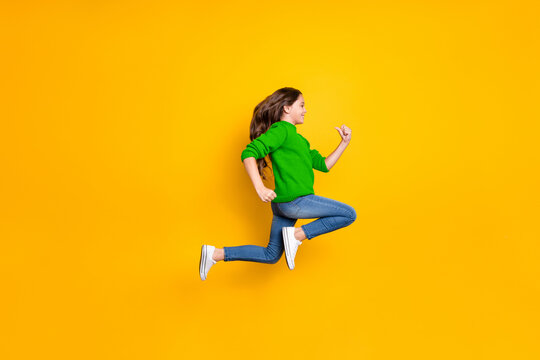 Full length profile side photo of positive cheerful brunette wavy curly hair kid jump run fast speedy after winter season discounts wear style clothes white sneakers isolated yellow color background