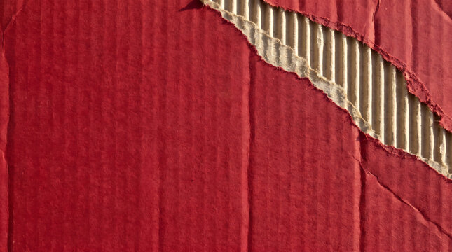 Red corrugated cardboard sheet with a torn corner showing ridged flutes in macro texture