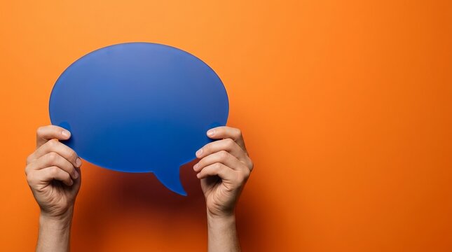 Two hands holding a solid blue speech bubble cutout against a vibrant orange background, representing communication, dialogue, and social interaction