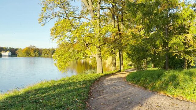 A winding pathway guides your view alongside a serene lake in Catherine Park, Pushkin, Saint Petersburg. Smooth forward motion creates a peaceful, relaxing feeling as you explore this scenic nature.