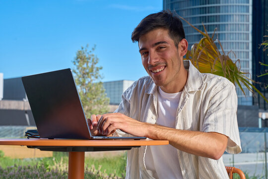 Young man smiling working outdoors on laptop