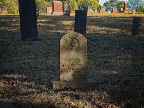 Weathered 19th century gravestone with hand carving pointing upward in historic cemetery bathed in warm sunlight