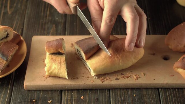 Hands slicing a filled sweet bread roll on a wooden cutting board, creating even pieces with a kitchen knife in a rustic tabletop food preparation scene