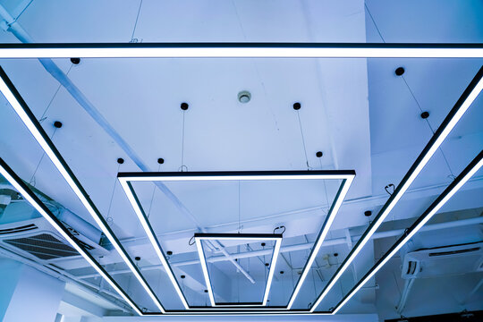 Geometric rectangular LED pendant lights hanging on ceiling with blue tone, modern office interior