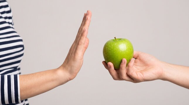 Woman rejecting fresh green apple offered by another person demonstrating dietary restriction allergy intolerance refusal healthy lifestyle choice concept indoor studio lighting