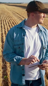 Smiling farmer operates with digital tablet in cut wheat field