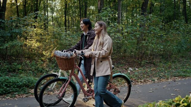Couple walks bicycles along peaceful autumn forest pathway