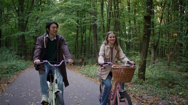 Smiling couple cycles together through green woodland trail