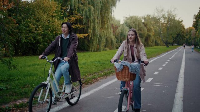 Couple cycles together on wide paved road through autumn park