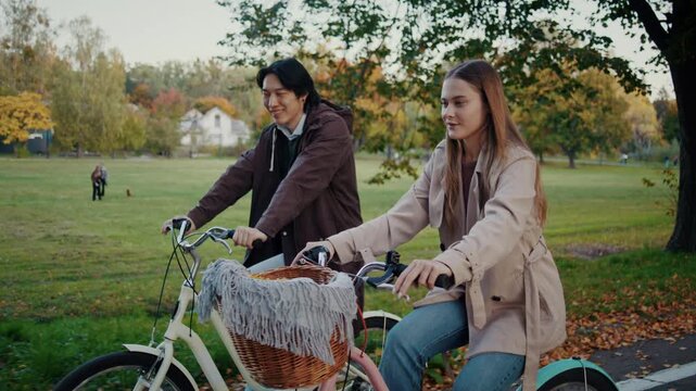 Smiling couple rides bicycles together through autumn city park