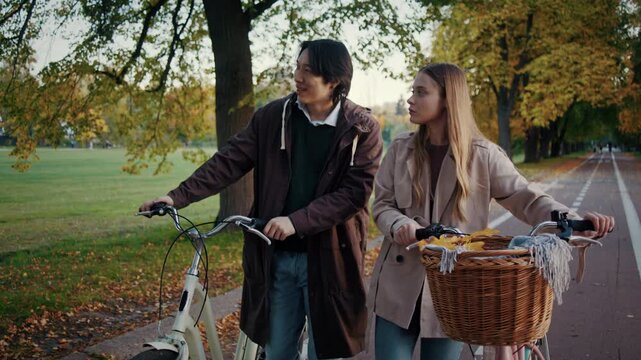 Couple walks with bicycles looking across autumn park path