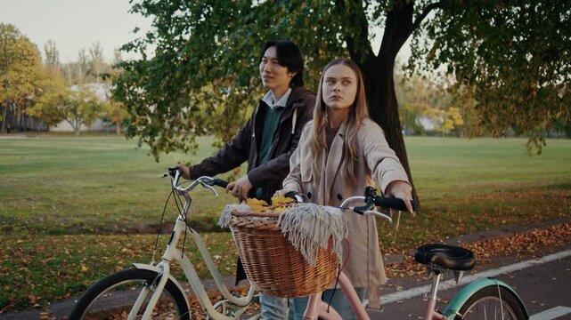 Couple walks bicycles together along peaceful autumn park path