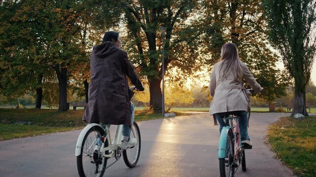 Couple cycles together through autumn park at warm sunset