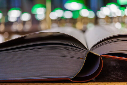 Open book with pages on wooden table in library with green lamp bokeh in background