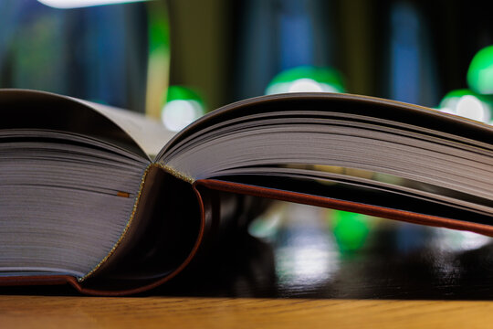 Open book with pages on wooden table in library with green lamp bokeh in background