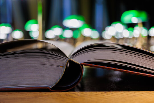 Open book with pages on wooden table in library with green lamp bokeh in background