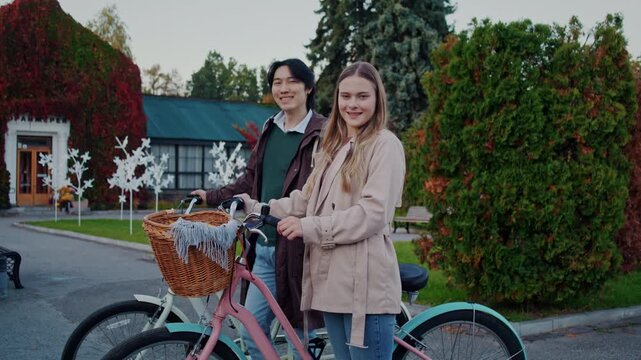 Smiling couple stands with bicycles near colorful garden house