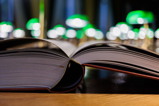 Open book with pages on wooden table in library with green lamp bokeh in background