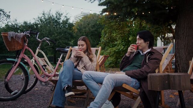 Couple relaxes with hot drinks near bicycles in city garden