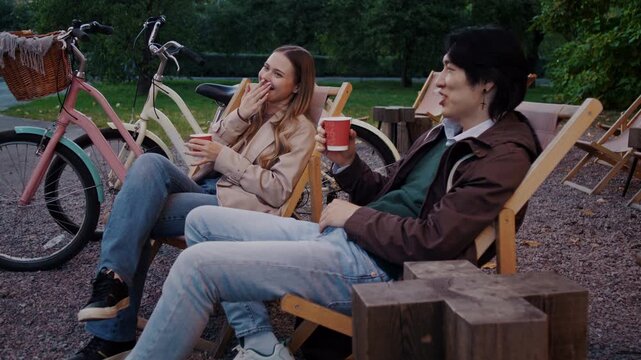 Woman gestures while couple relaxes with hot drinks in garden