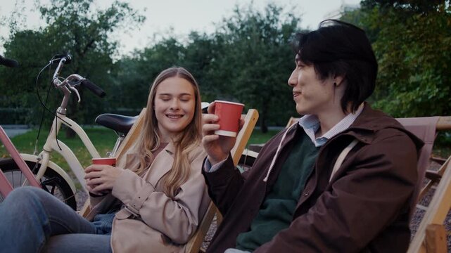 Smiling couple raises red cups of tea during relaxed park break