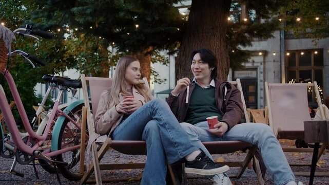 Couple talks holding drinks as resting near bicycles outdoors