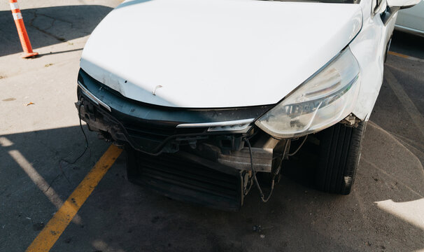 A white car has a missing front bumper cover, exposed wiring and a dented hood. Visible damage illustrates vehicle repair, insurance claims and maintenance costs.