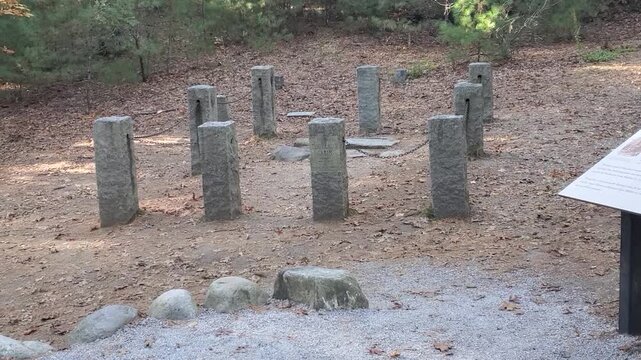 A panning video shot showing the historic site of Henry David Thoreau's cabin outlined by granite stone posts, accompanied by an informational interpretive sign and a large mound of visitor-stacked st