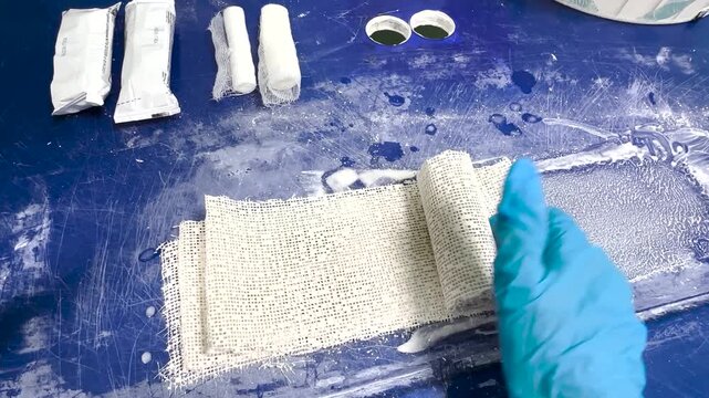 Doctor in medical gloves rolling plaster bandage on table for cast application