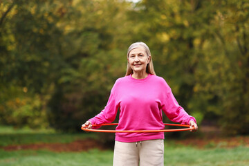 Senior woman exercising with hula hoop outdoors, space for text © New Africa