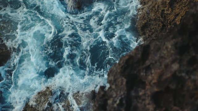 Foaming Surf Swirls Around Jagged Rocks On Nusa Dua Coast. Blue Water Rushes Into Narrow Channels Between Dark Stone Formations, Creating Energetic Patterns Of White Sea Spray.