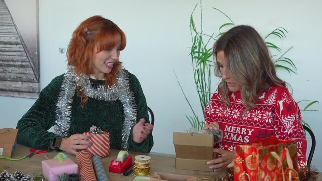 Cheerful friends wrapping and opening christmas gifts together at table