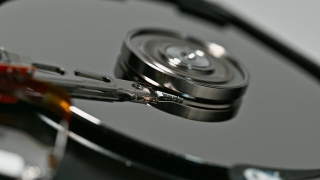 Close up of a hard disk drive mechanism with intricate components reflecting light. Precision engineering for data storage technology and device functionality.