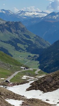 View down from Klausen Pass towards Linthal, Switzerland, during spring pass opening, with alpine road, green slopes and traces of snow in higher elevations.