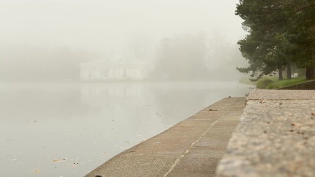 The Grotto Pavilion stands hidden in heavy fog across a quiet lake. Granite steps stretch along calm water, creating a peaceful atmosphere. This serene spot Catherine Park, Pushkin, Saint Petersburg.