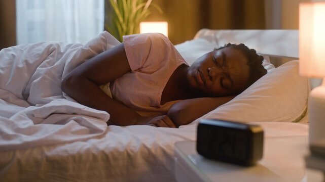 Disturbed African American woman waking up in bed checking alarm clock at night frustrated tired female girl suffering insomnia look time display sleeping indoors bedroom sleep problem exhaustion
