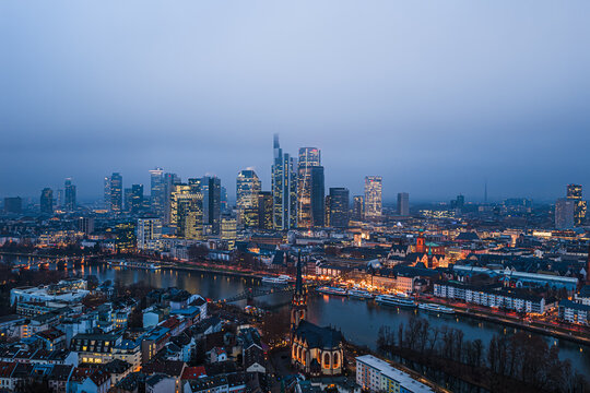 Aerial view over Sachsenhausen, the Main River and the Eiserner Steg toward the illuminated banking district at blue hour on a misty winter evening, Frankfurt, Germany