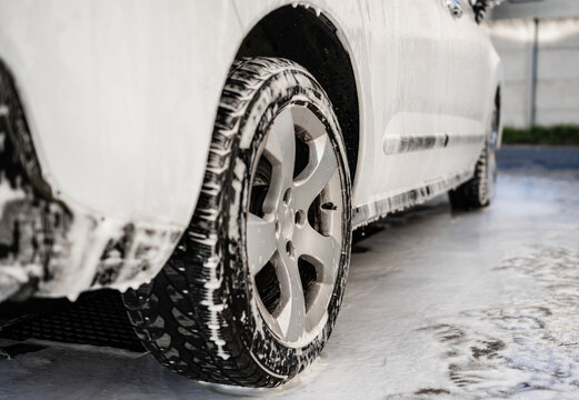 White car covered with soap suds during washing process
