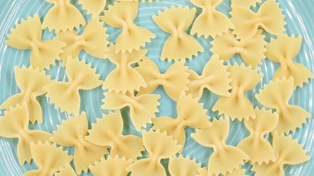 Uncooked Italian Farfalle, butterfly or bow tie pasta, close-up on a blue plate, rotating video.