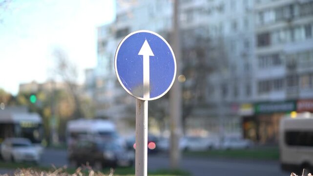 Blue circular mandatory direction sign with white upward arrow on city street pole.