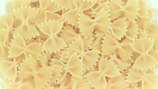 Uncooked Italian Farfalle, butterfly or bow tie pasta, extreme close-up on a white plate, rotating video.